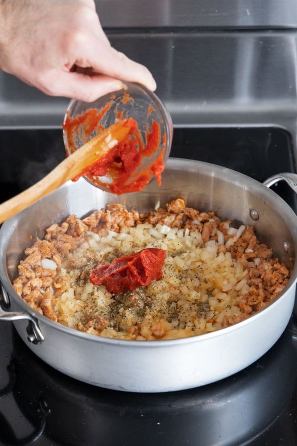 Adding tomato paste to skillet along with sausage and onion.