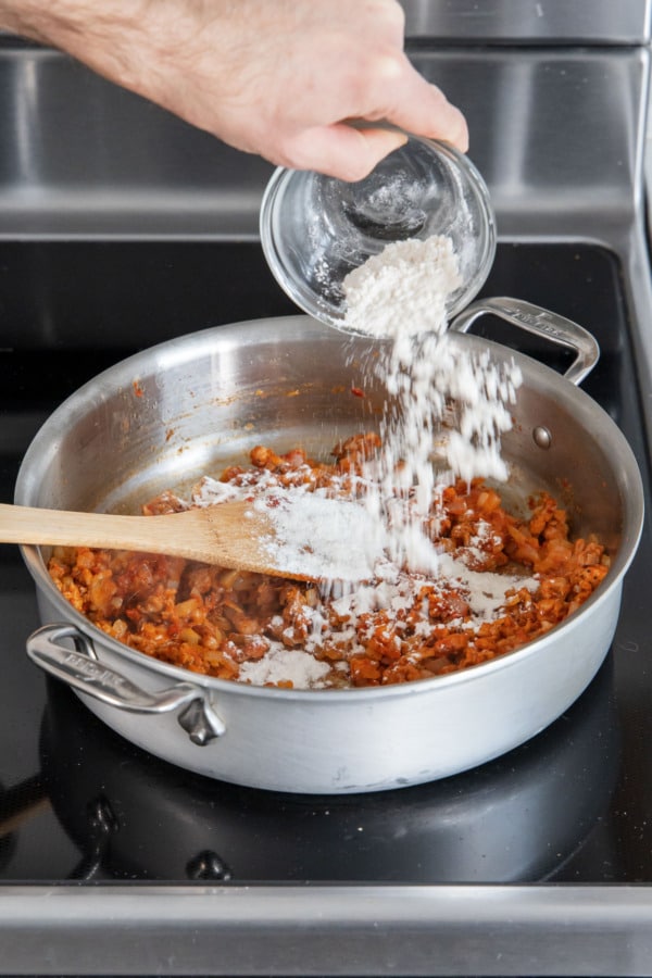 Adding flour to skillet along with cooked sausage mixture.