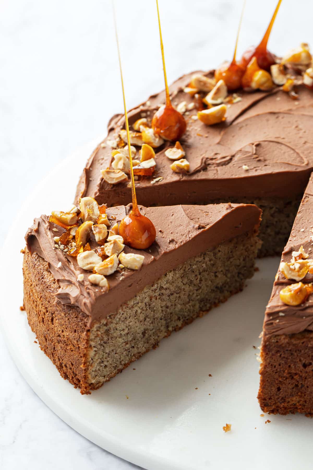 Flourless Hazelnut Cake with Nutella Whipped Ganache on a flat marble cake plate with one slice cut and pulled out slightly to show a cross-section.