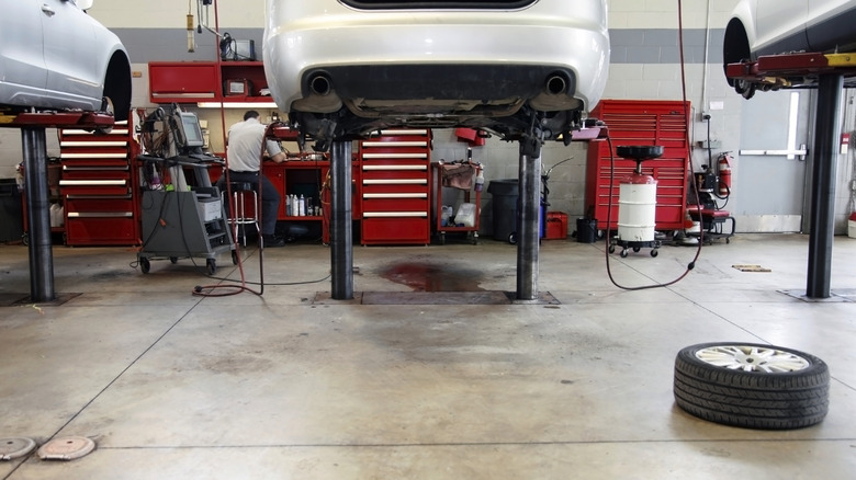 The interior of a car dealership repair facility, shows two cars on hoists.