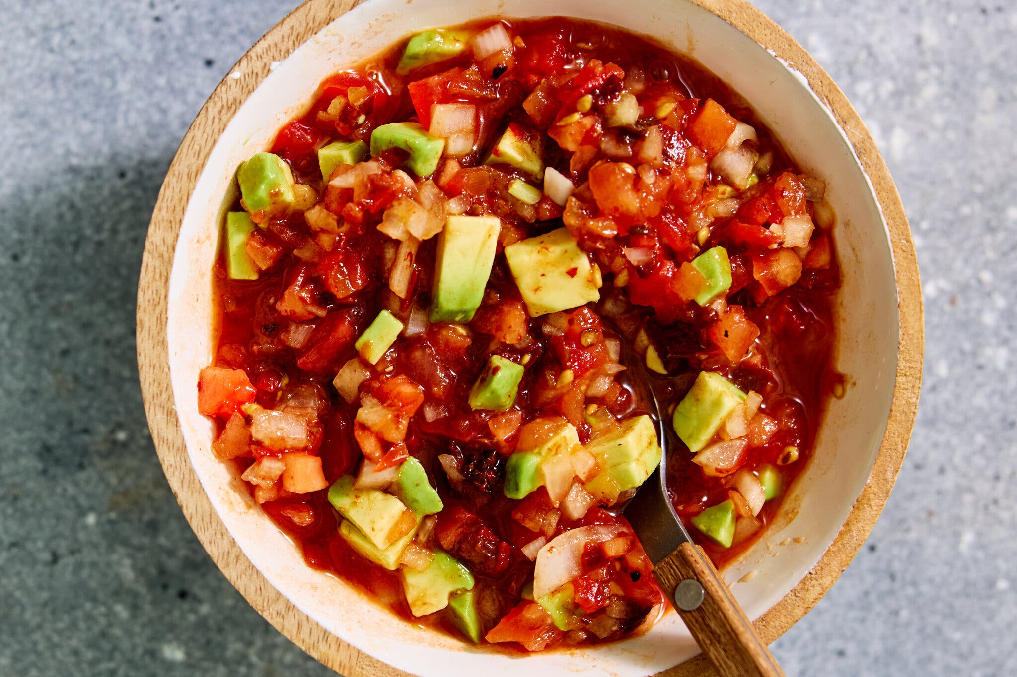 An overhead image of a chunky red salsa in a bowl, dotted with cubes of avocado.