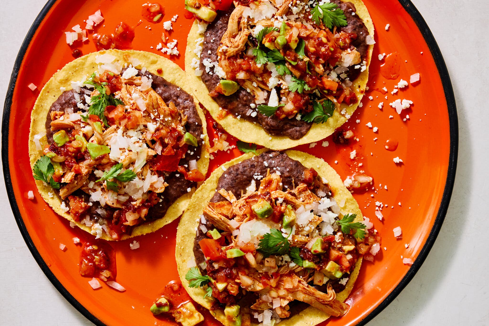 An overhead image of three tostadas on a platter, topped with beans and chicken.