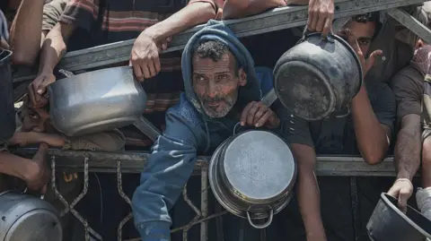 Anadolu via Getty Images People wait to receive aid food in Gaza City. Photo: 30 July 2025