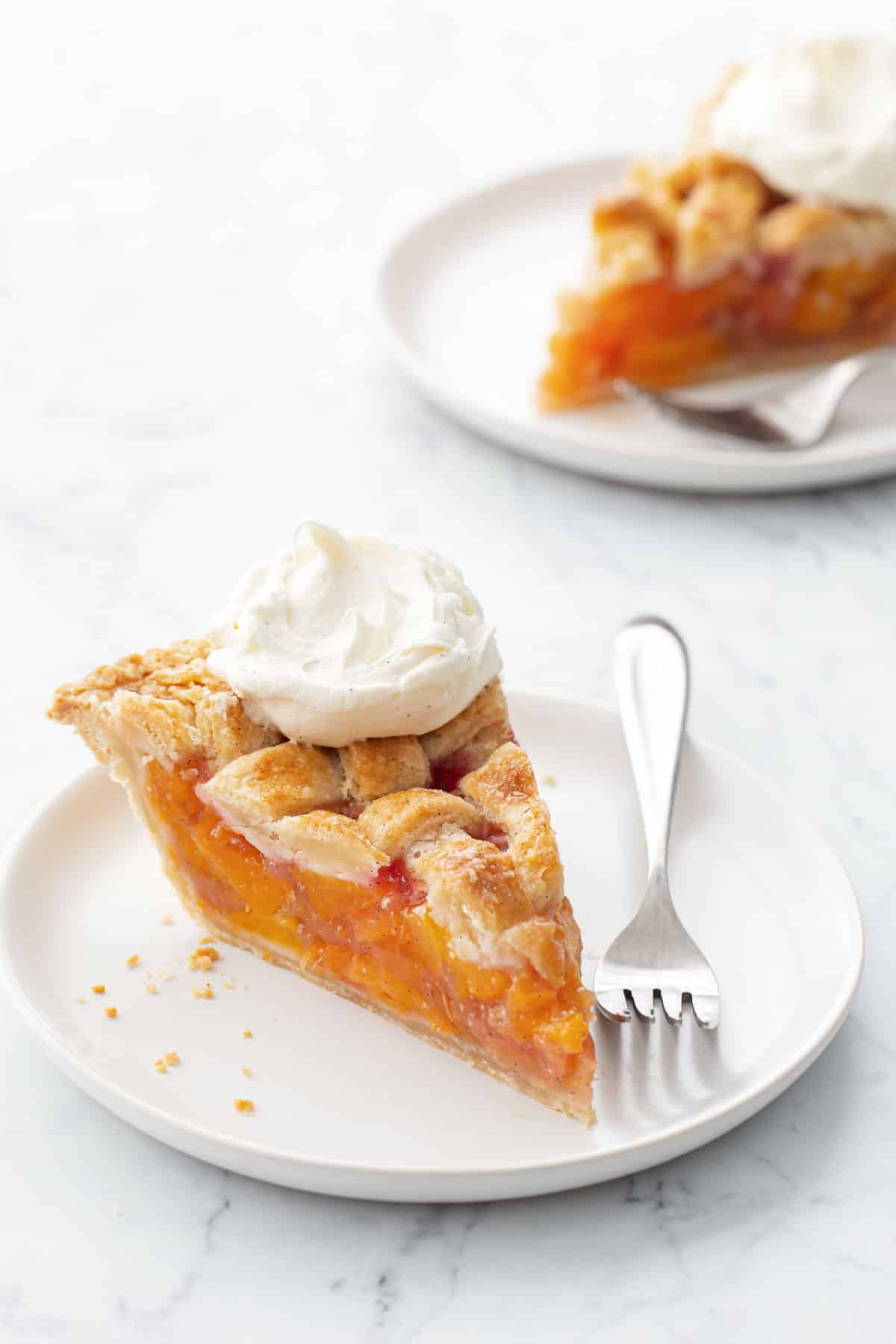 Slice of Vanilla Bean Peach Pie on a white plate with fork and dollop of whipped cream.
