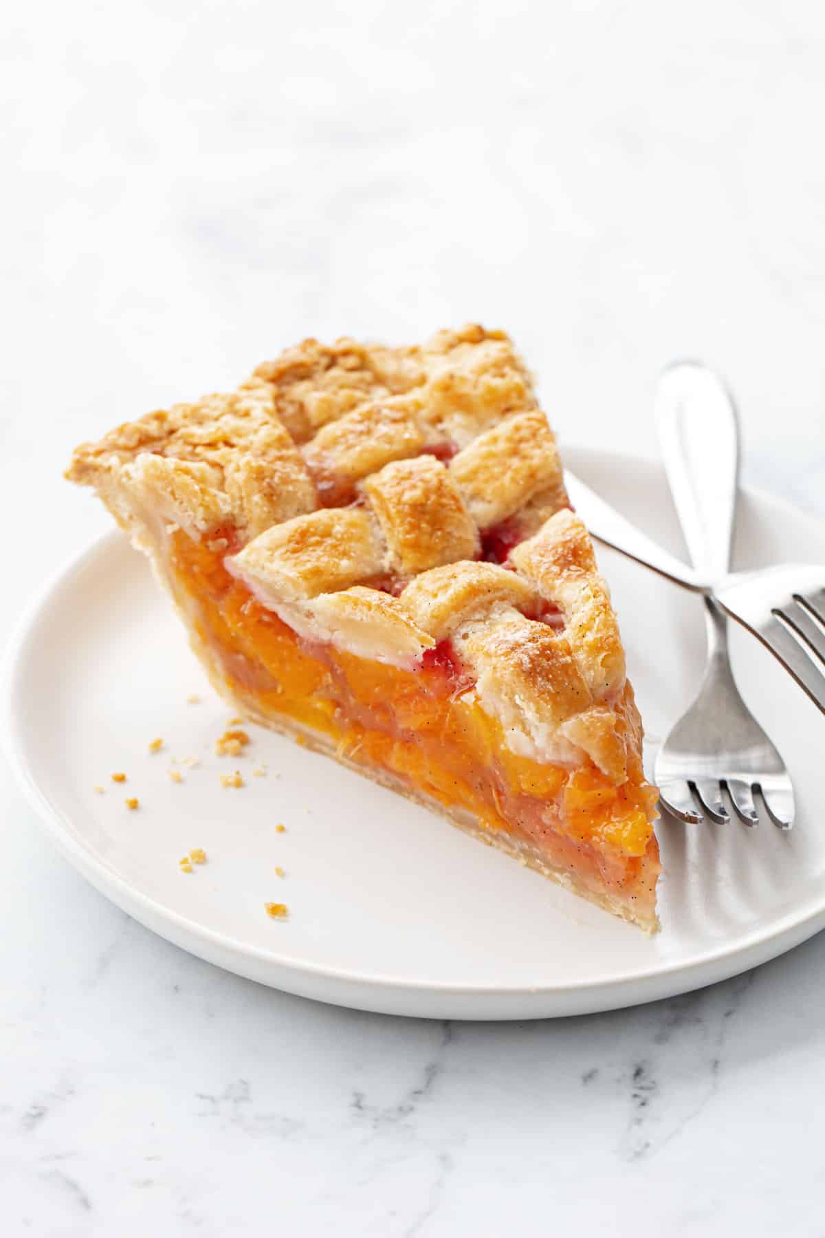 Slice of lattice-topped Vanilla Bean Peach Pie on a white ceramic plate with two silver forks.