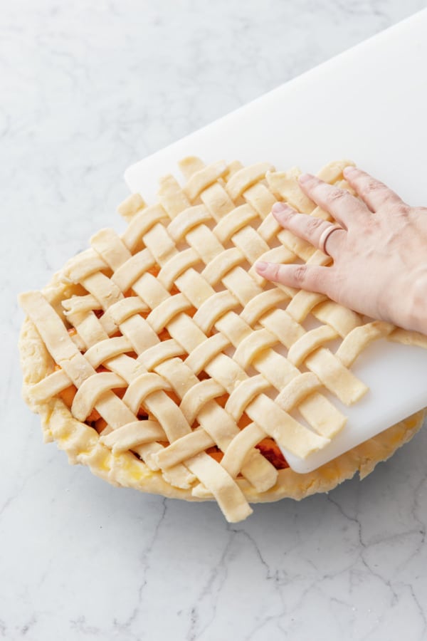 Sliding a pre-assembled lattice crust top onto filled pie before baking.