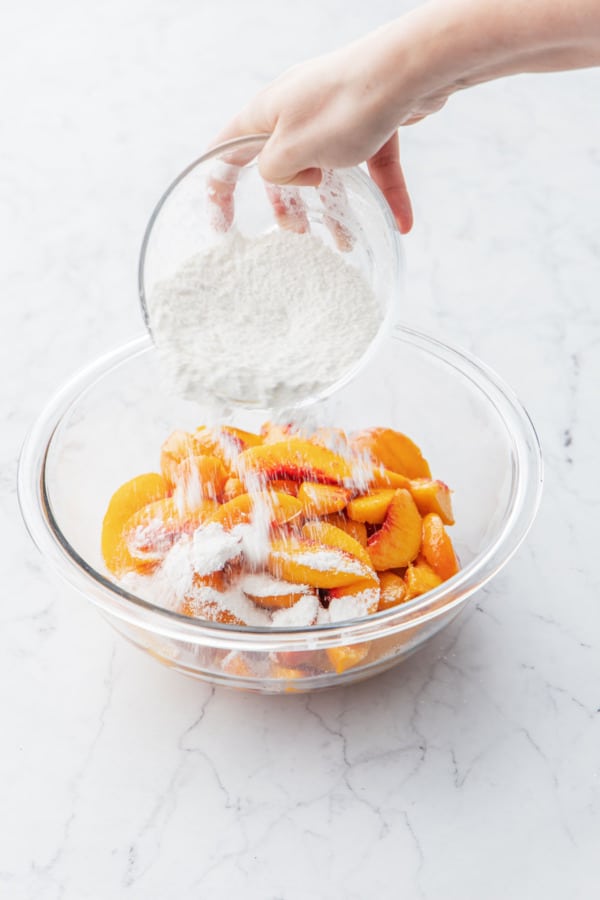 Sprinkling cornstarch-sugar mixture over the top of the cut peaches in a glass bowl.