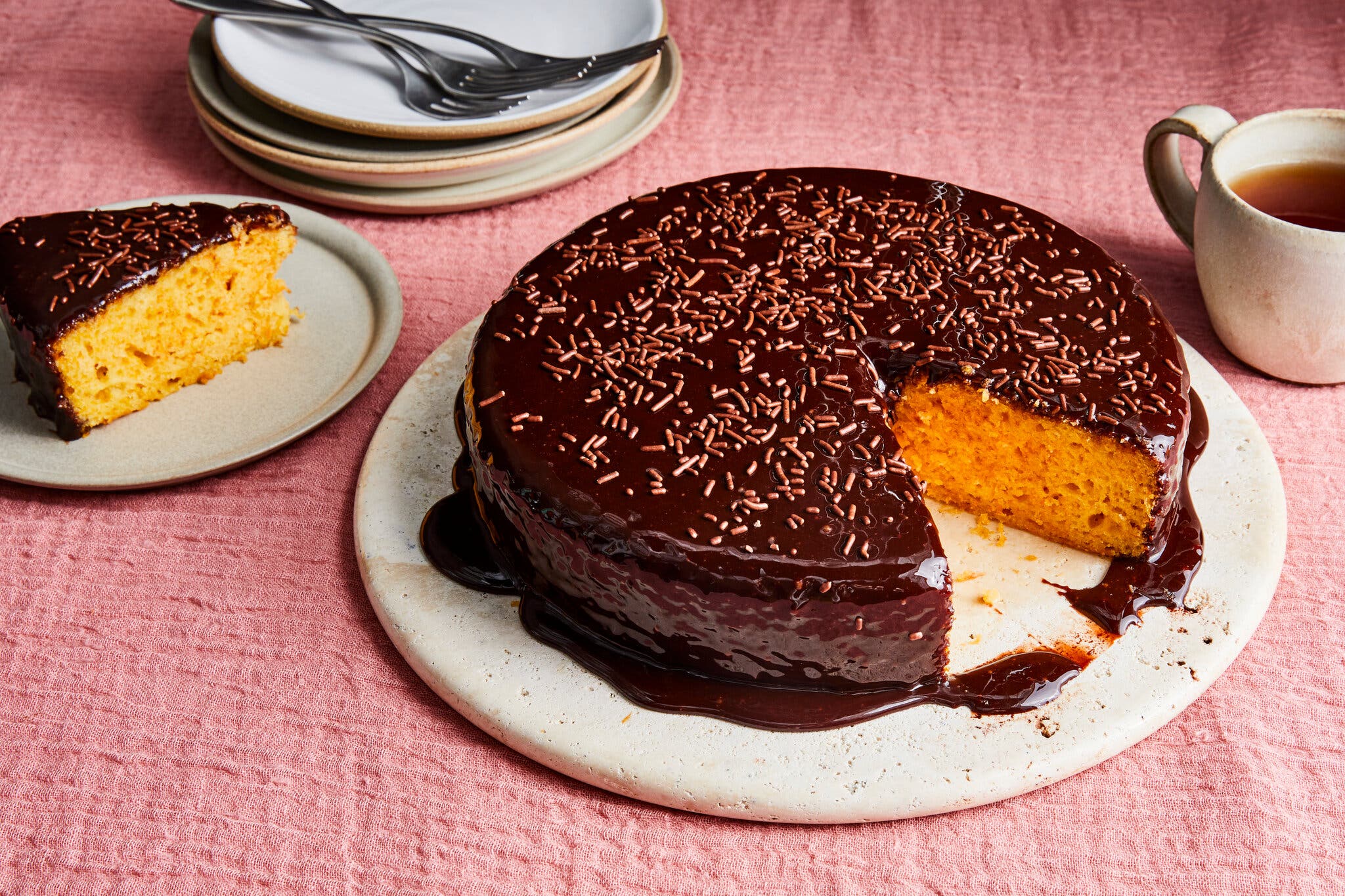 A chocolate-covered carrot cake is photographed at an angle. A single slice is taken out and set to the side.