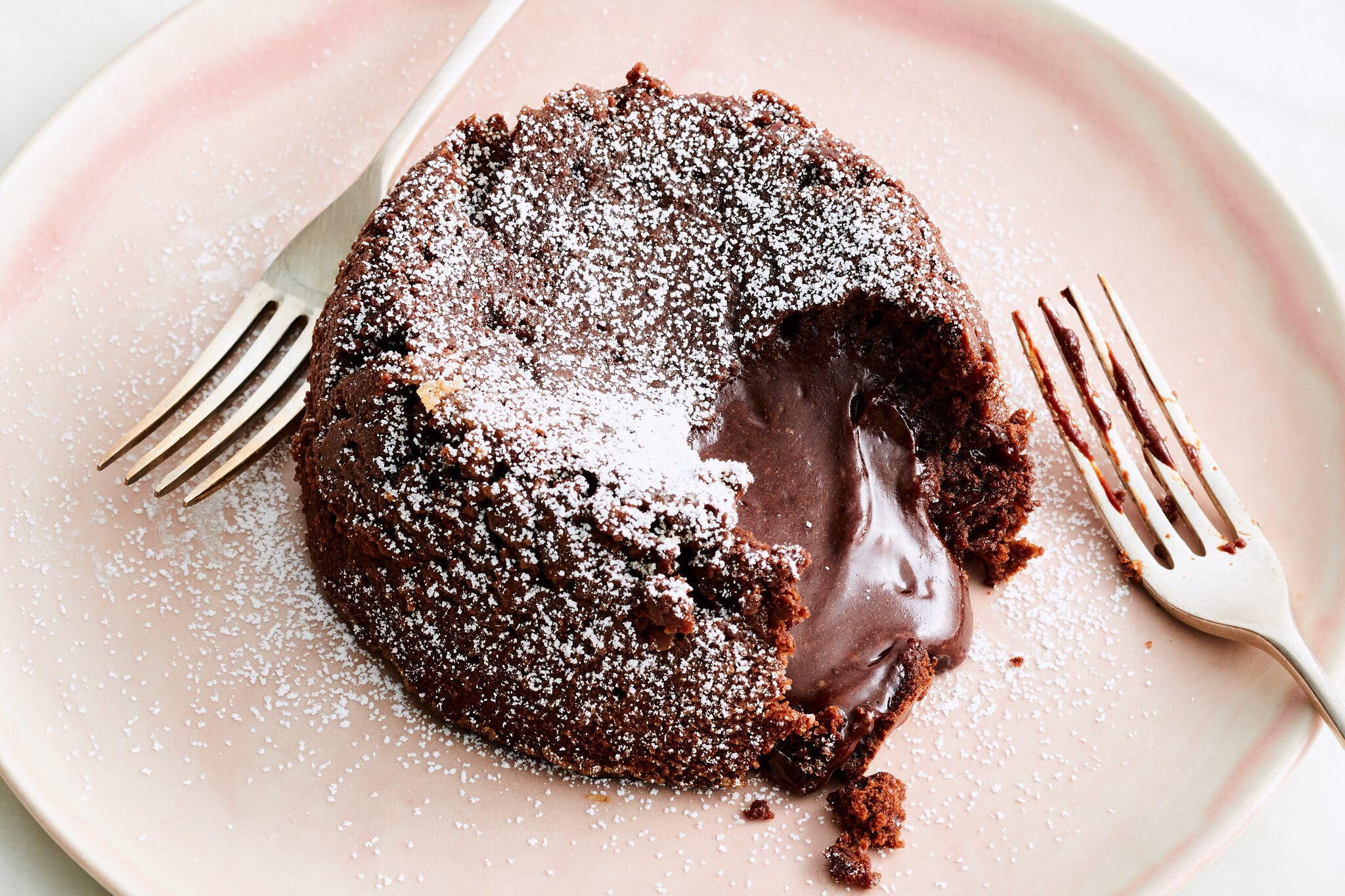 An overhead image of a cake with a bite taken out and chocolate oozing onto a plate.