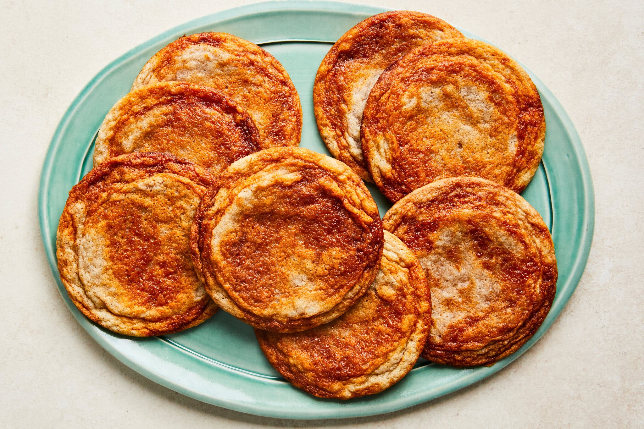Eight reddish sugar cookies sit on a mint-green plate.