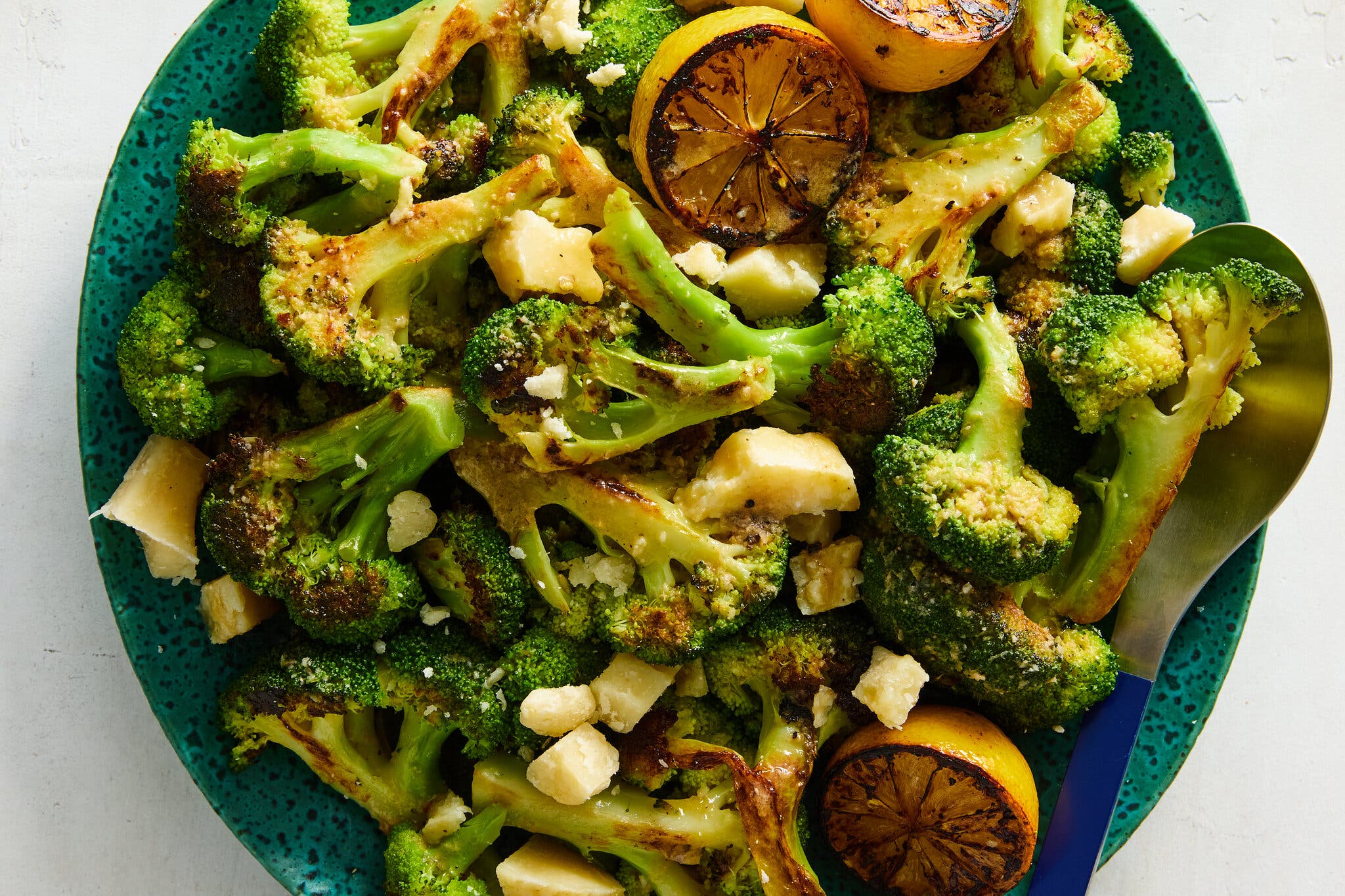 A green plate of roasted broccoli includes chunks of Parmesan.
