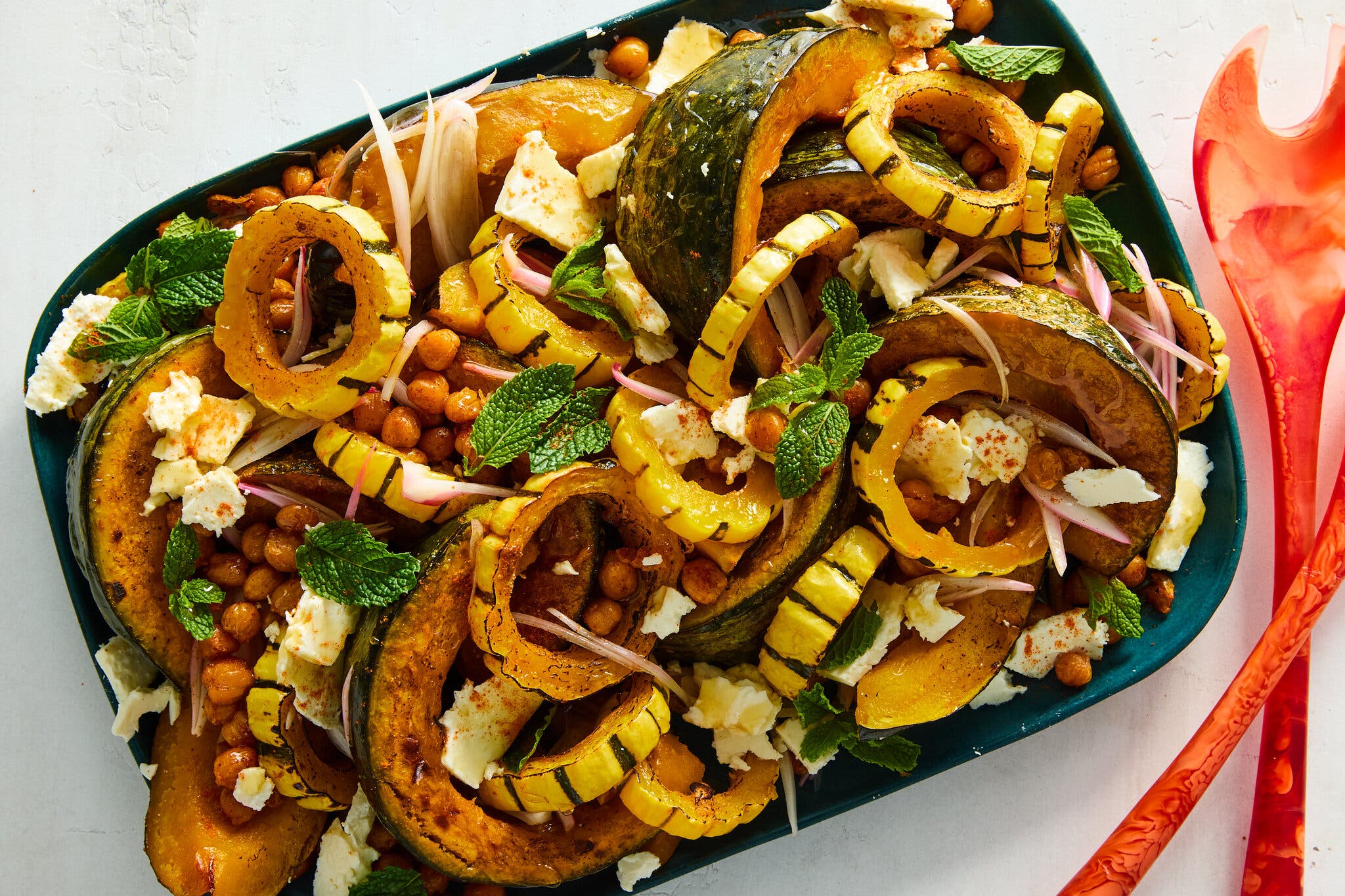 A rectangular blue platter holds roasted squash, chickpeas, herbs and feta.