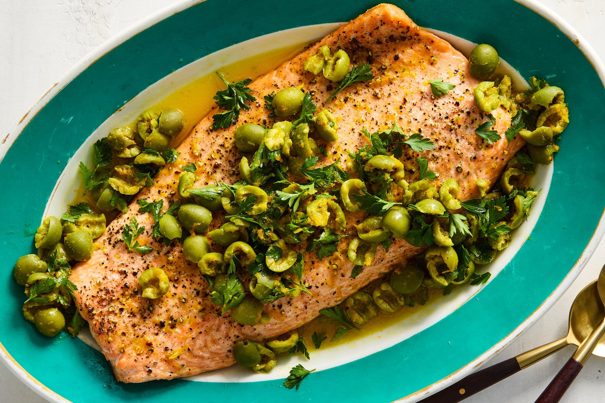 An oval platter cradles a whole fillet of salmon topped with cracked green olives and herbs.