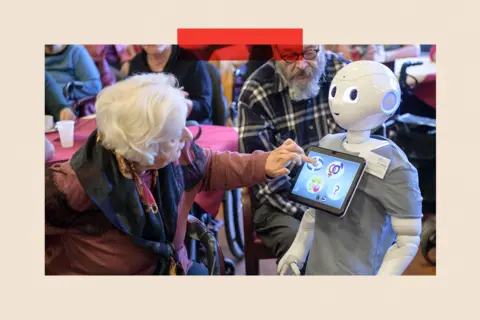 Getty Images An elderly woman looks to a robot and touches the screen on its front