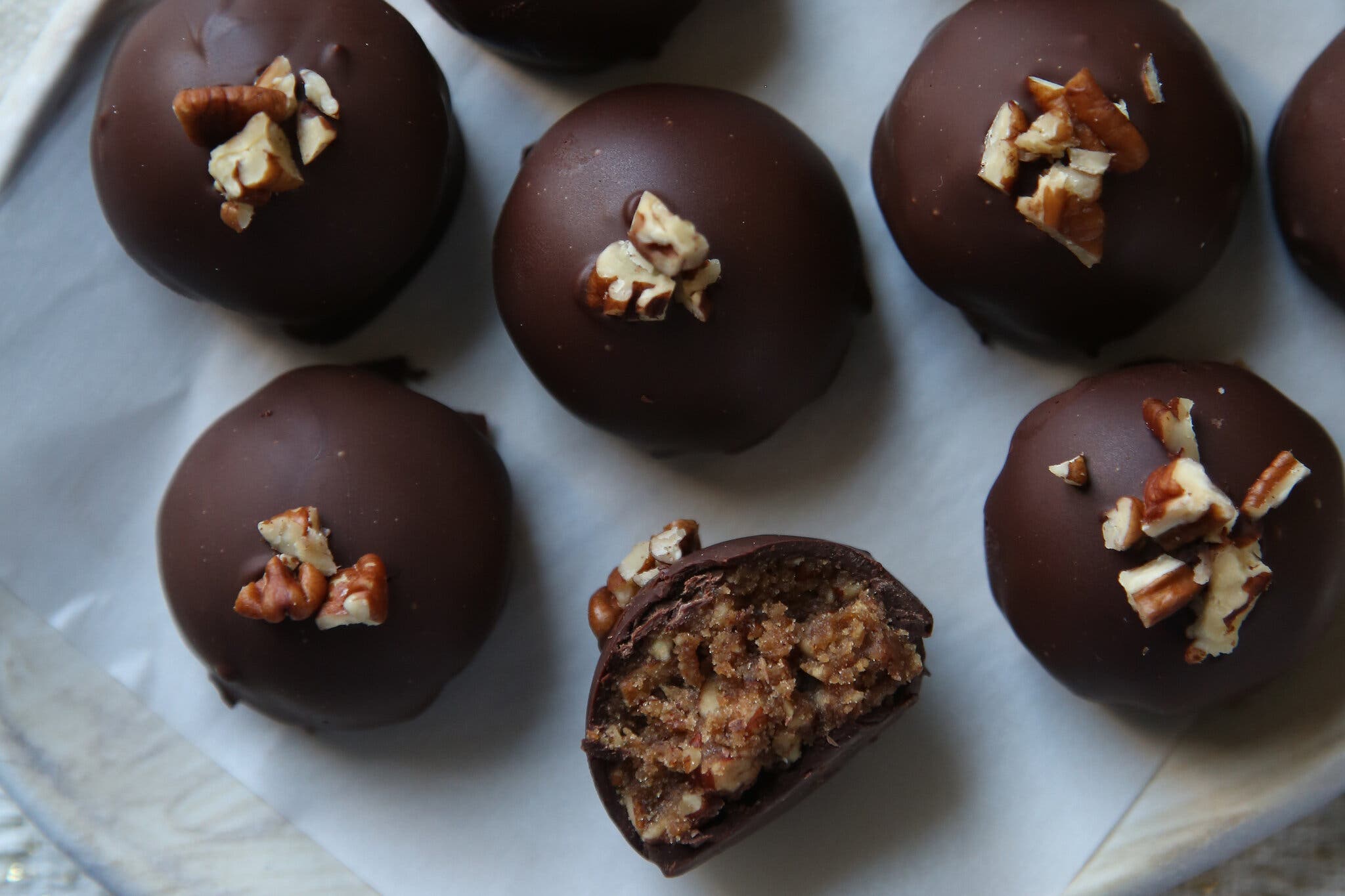 An overhead close-up of chocolate-coated pecan pie truffles. One of the truffles is turned on it’s side and bit in half revealing its filling.