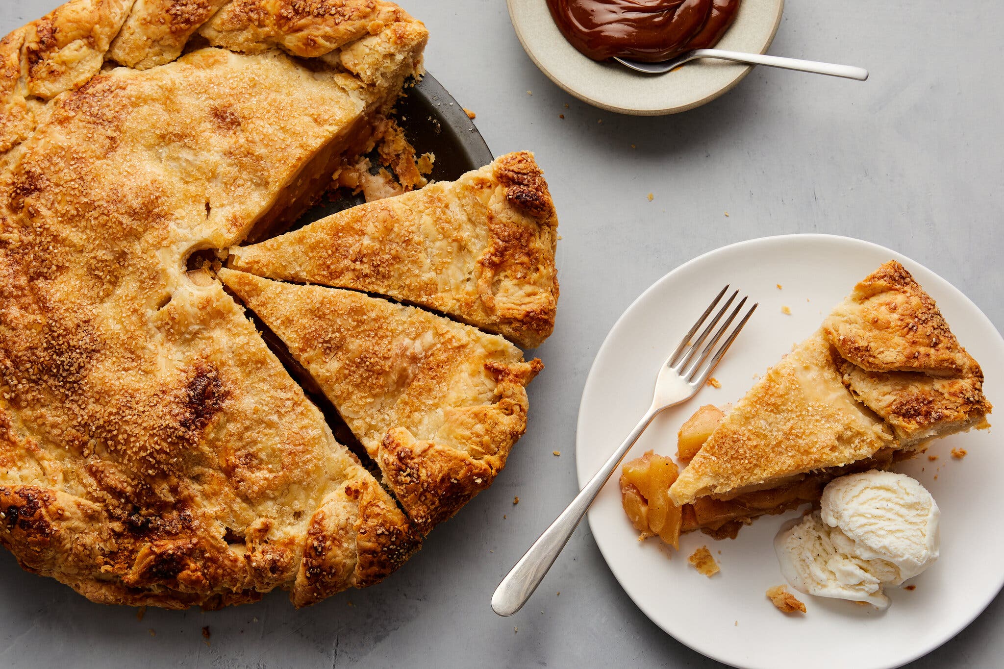 An overhead image of apple pie. To the bottom right of the frame sits a plate with a slice of pie and a scoop of vanilla ice cream.