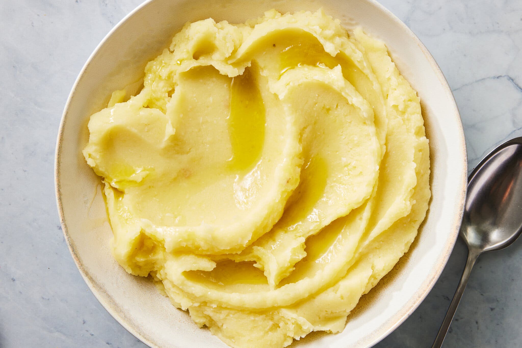 An overhead image of a white bowl full of swirled potatoes. Butter pools between the swirls.