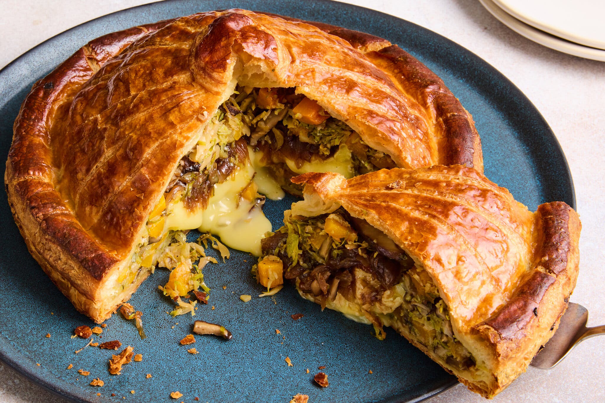 A phyllo pie filled with brie and vegetables is photographed from the side. A slice has been cut out, and cheese oozes out.
