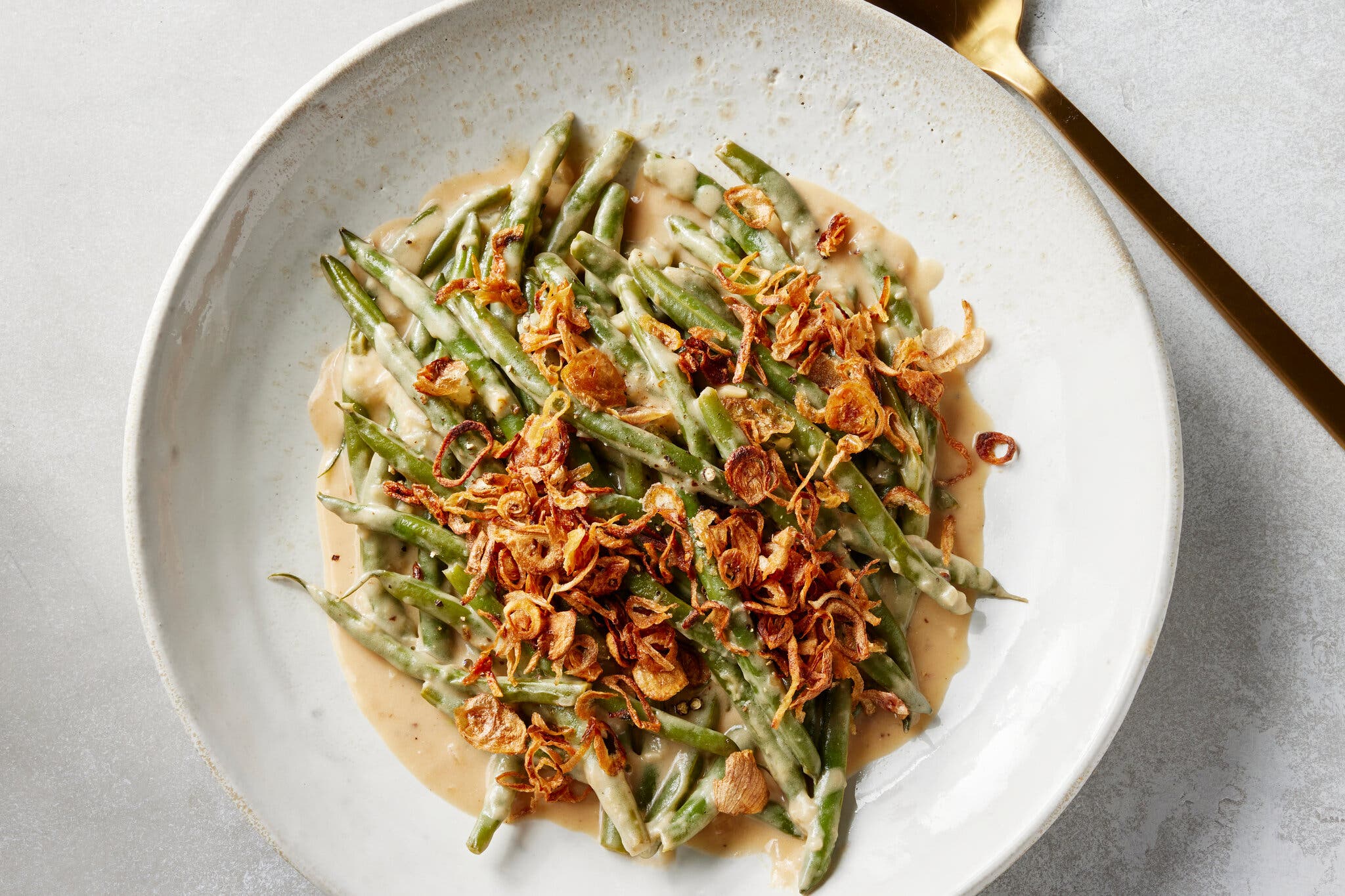 An overhead image of crispy shallot topped green beans in sauce.