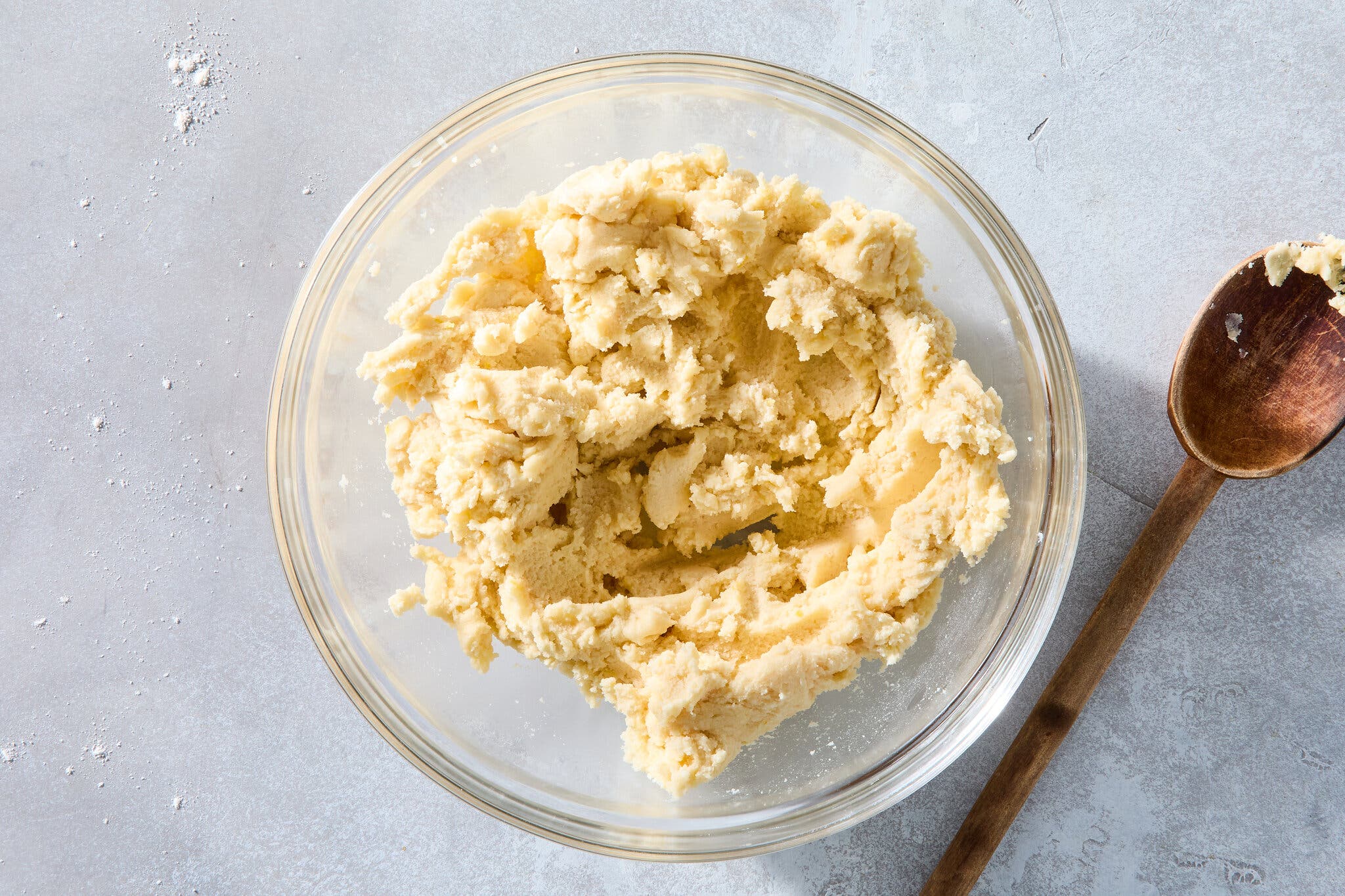 An overhead image of dough in a glass bowl. A wooden spoon sits off to the side.