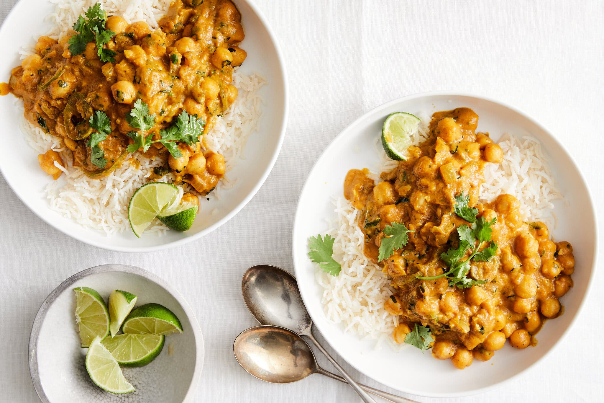 An overhead shot of two white bowls filled with rice and coconut curry chickpeas with pumpkin and slices of lime.