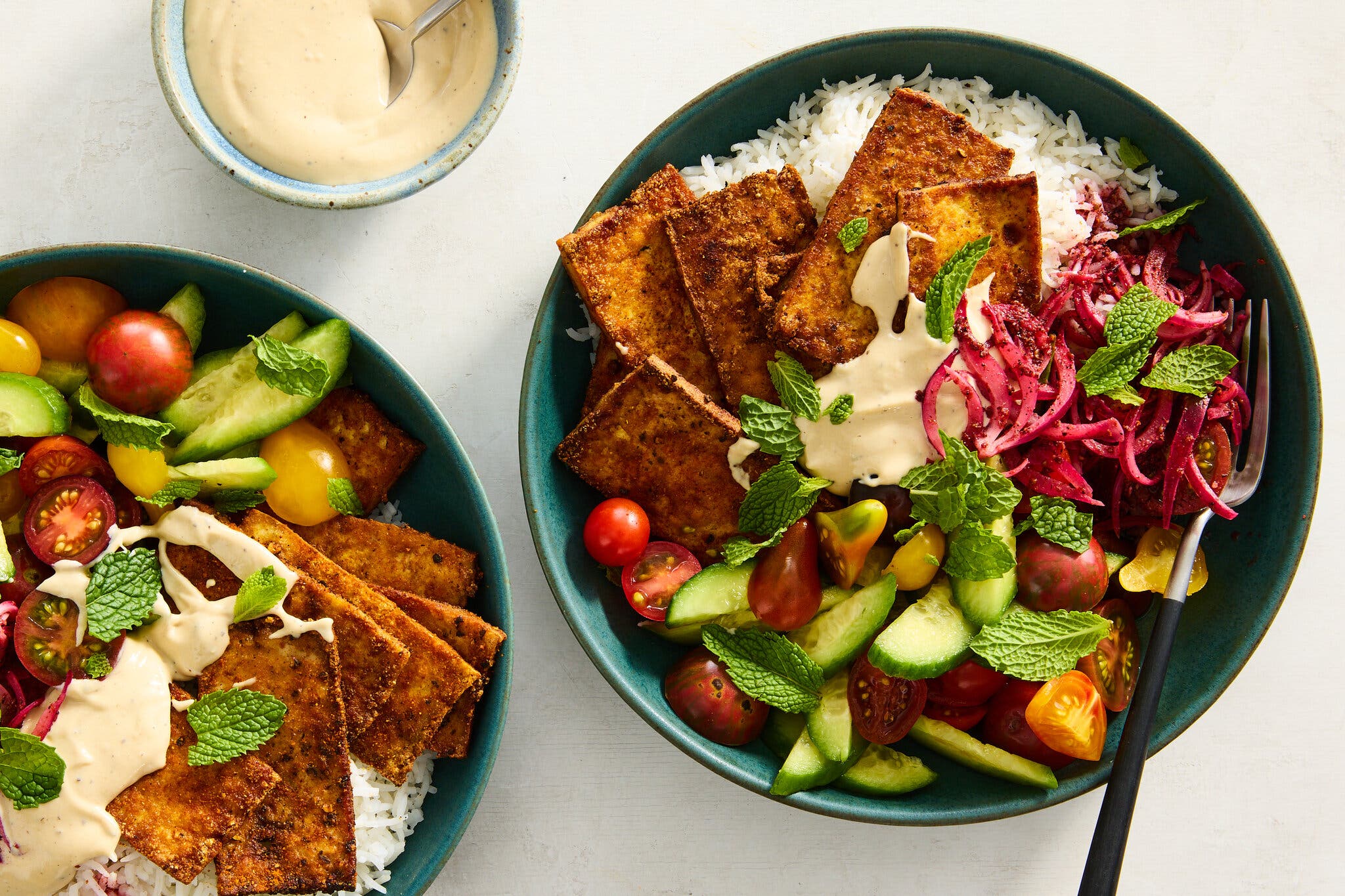 An overhead image of thin slabs of tofu topping rice and with a salad of cucumbers and tomatoes.